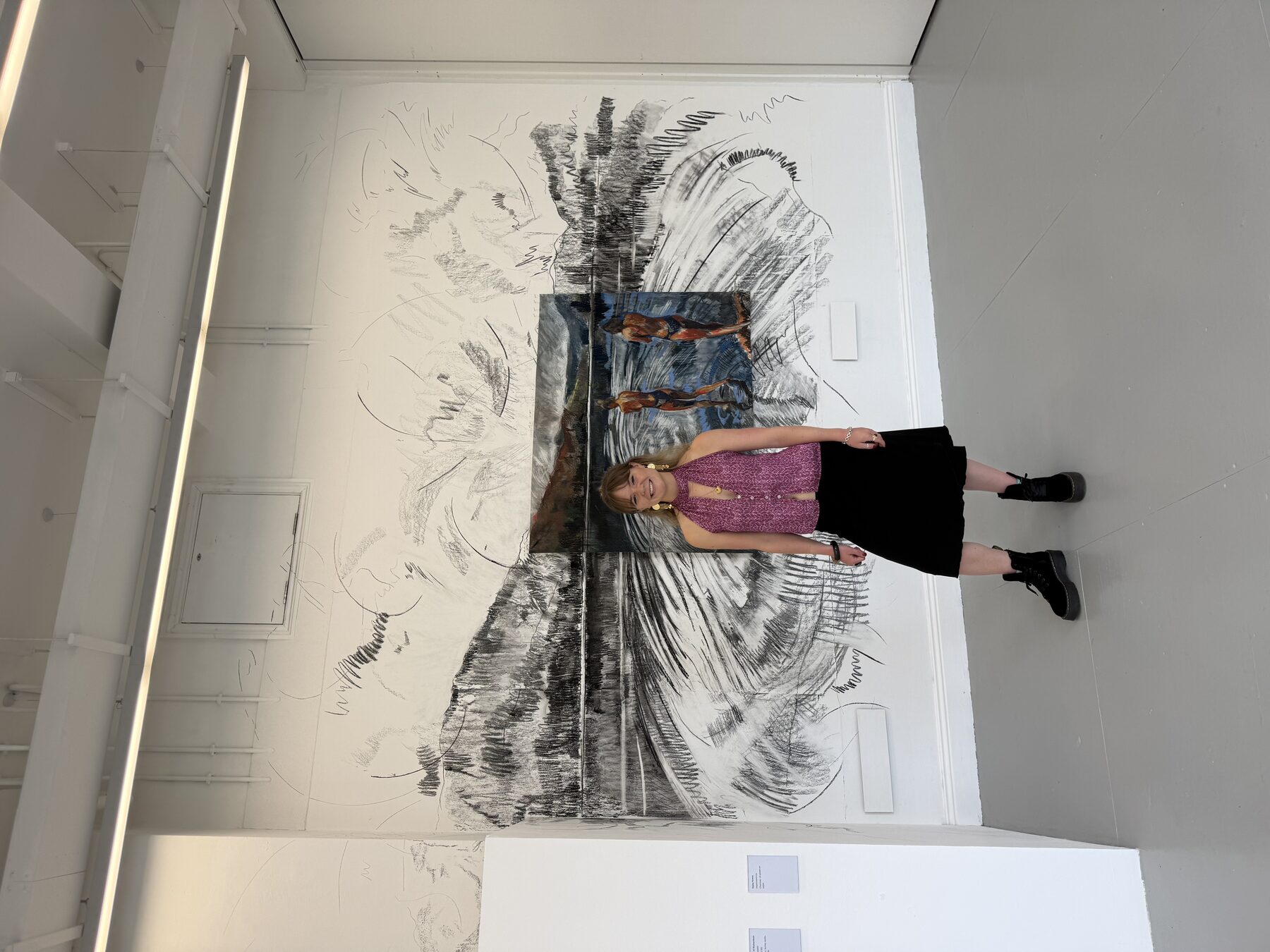 Daisy Krens standing in front of her charcoal and pastel work in a gallery